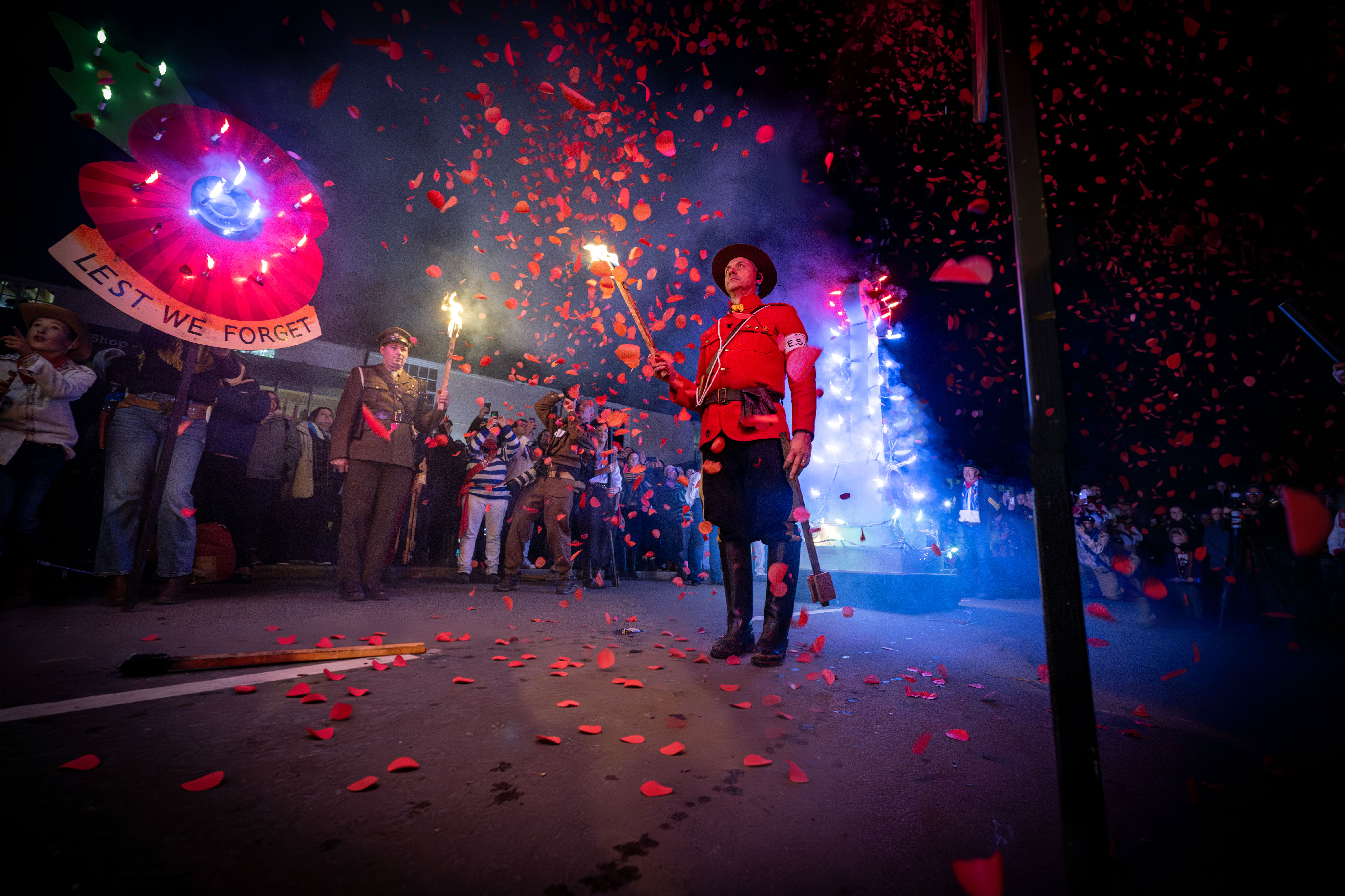 Remembrance-themed display at the East Hoathly Carnival and Bonfire celebrations, featuring a large illuminated poppy, torchbearers and falling red petals during the evening procession.